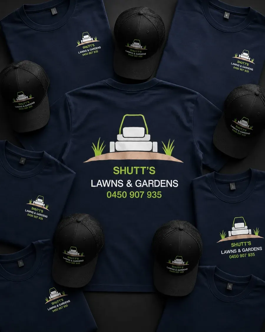 Navy Shutt's Lawns and Gardens work shirts and black caps laid out with the logo and phone number